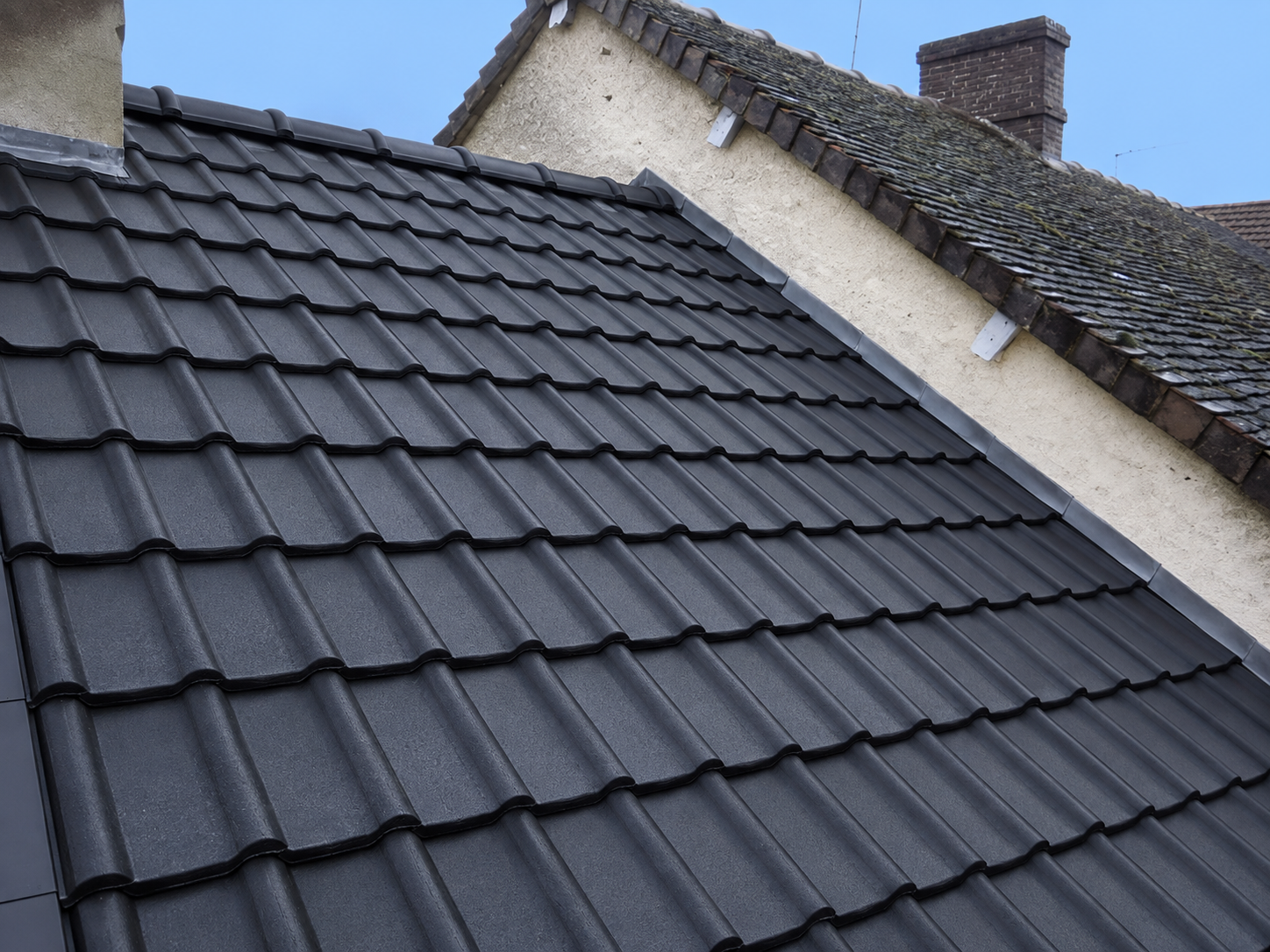 Toiture en tuiles anthracite tout juste achevée, avec solin en zinc le long du mur